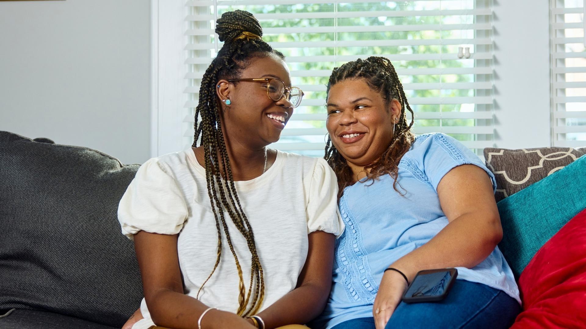 Two people sitting closely on a sofa smiling and looking at each other.