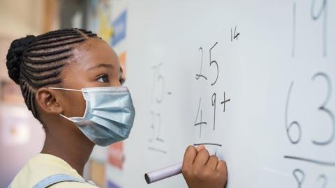 Child with mask on solving a math problem on a whiteboard