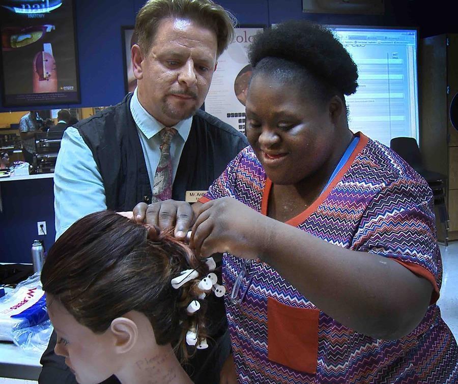 A woman styles another woman's hair as a man watches. 