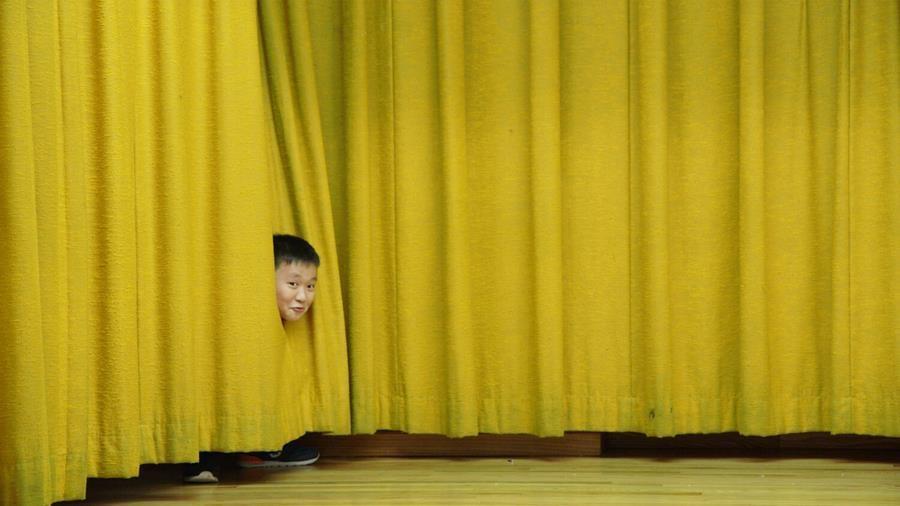 A boy peeking through stage curtains.