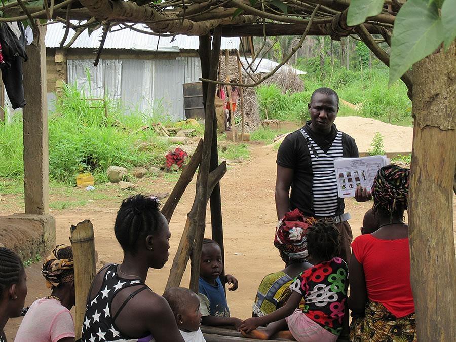 a man holding up a bunch of papers talks to a group of people seated in front of him