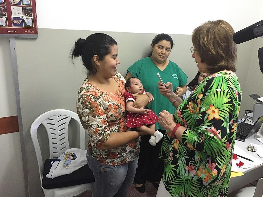 a woman holds a baby with a small head as another woman examines the baby