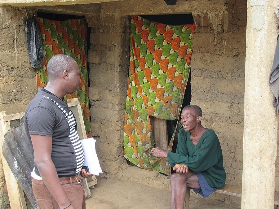 a man holding some papers talks to a person seated on a bench