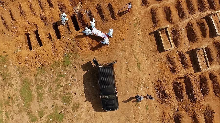 aerial view of men wearing full-body coveralls bringing a body to an open grave site