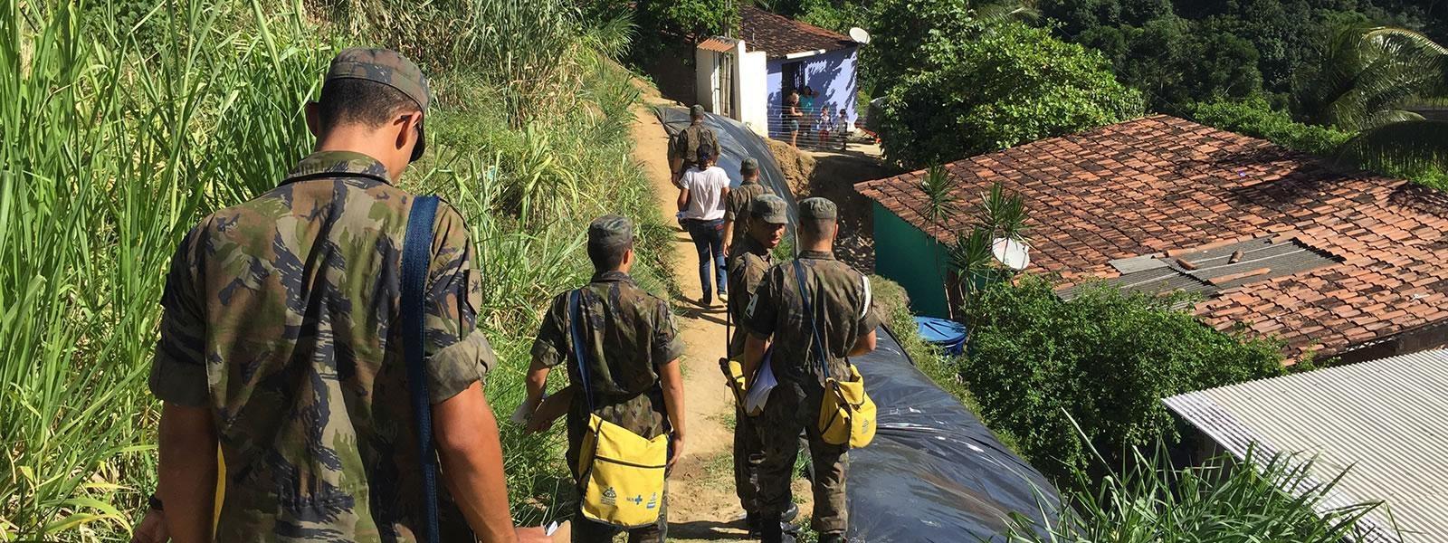 Soldiers  carrying medical supplies walking down a path toward houses