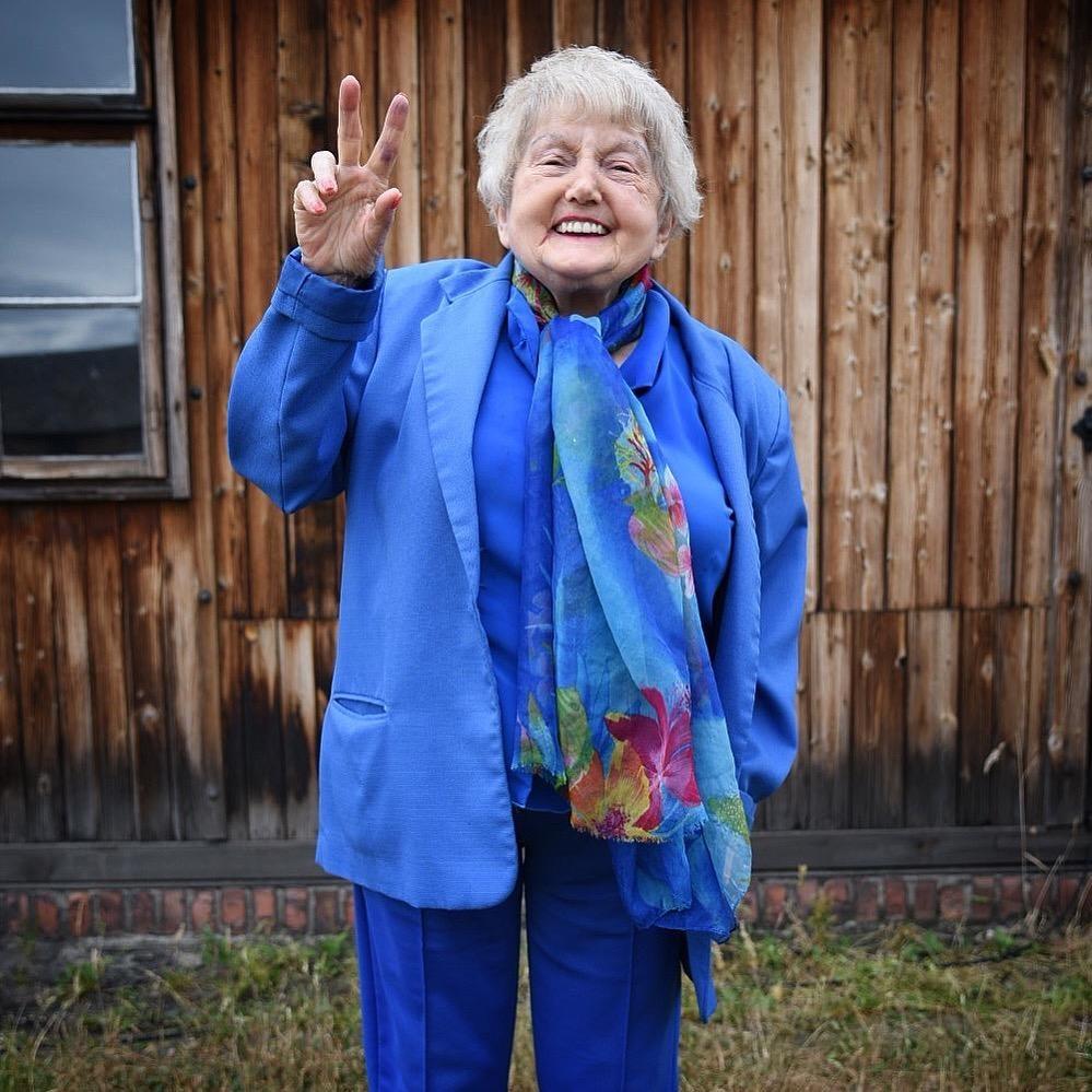 Eva Kor smiles while making a peace symbol with her hand.