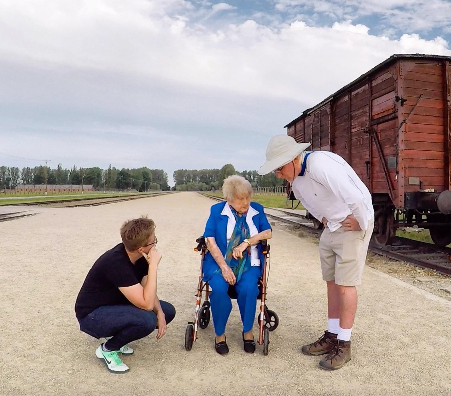 Filmmakers Ted Green and Mika Brown kneel to talk with Eva Kor at Auschwitz.