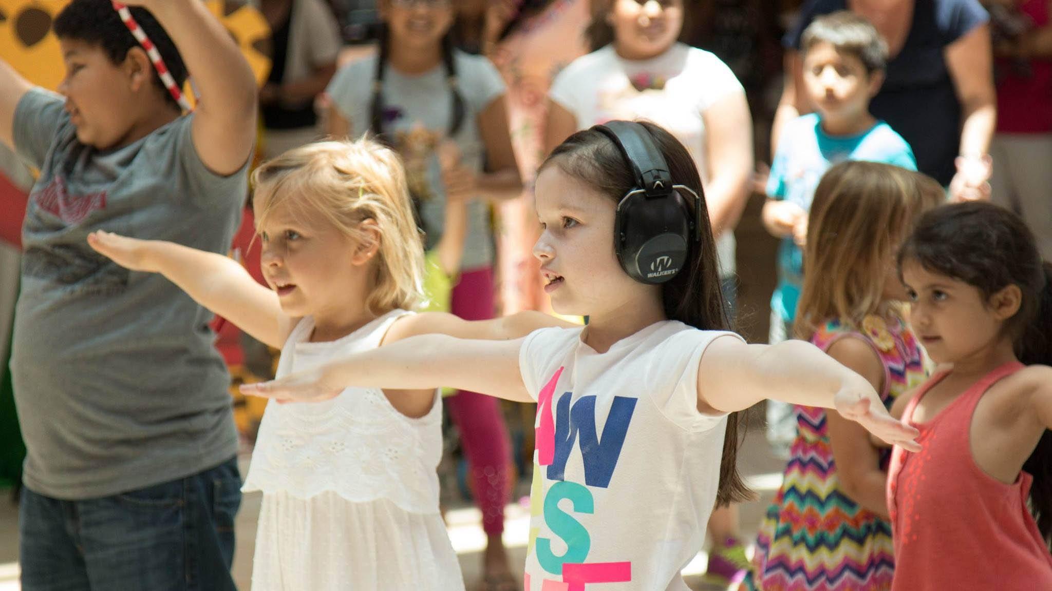 A group of children outside with arms outstretched, participating in a group activity.