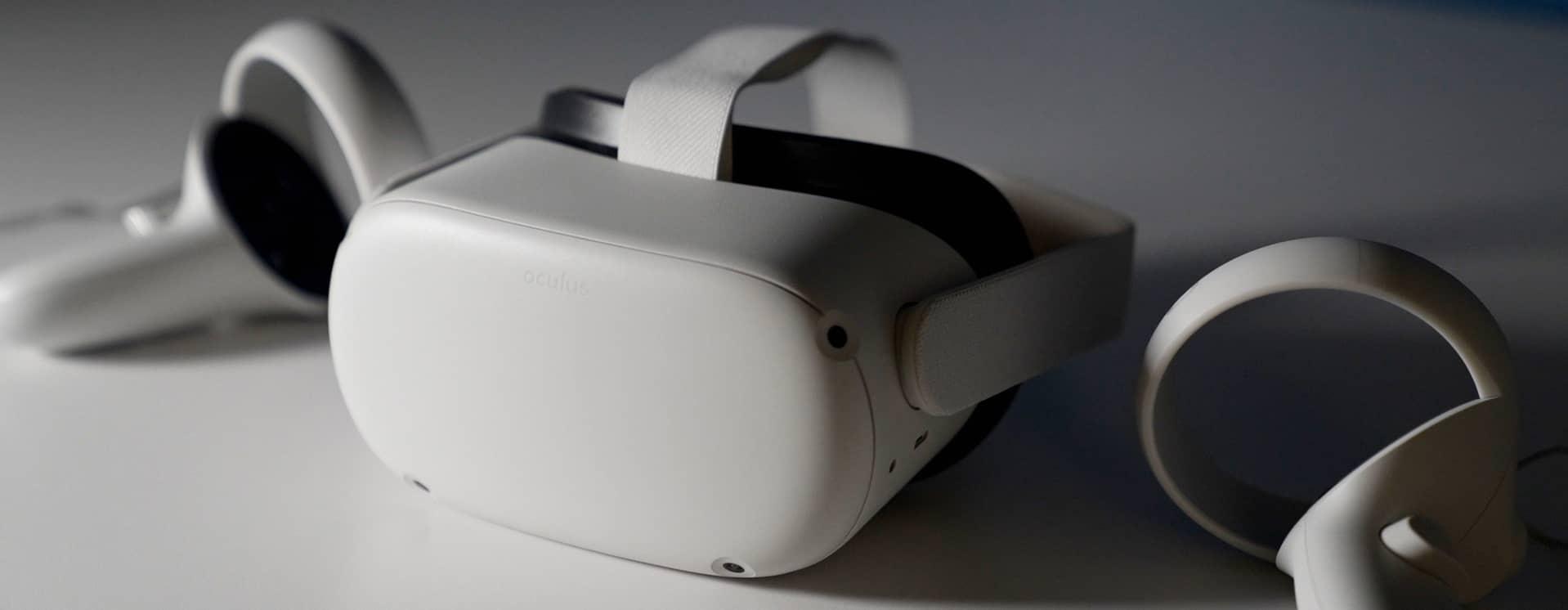 White Oculus brand VR head set on white table top with hand controllers and dramatic lighting.