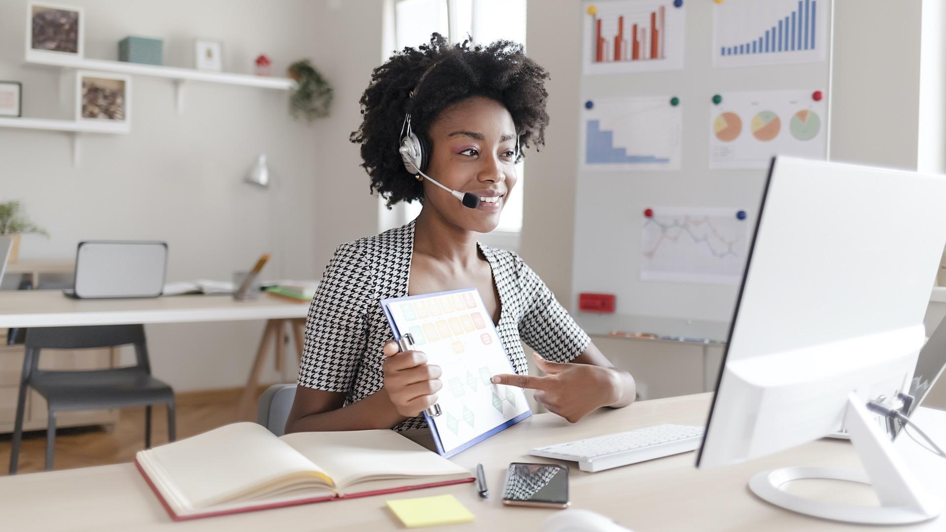 Teacher wearing a headset points at learning materials in her virtual lesson at her computer