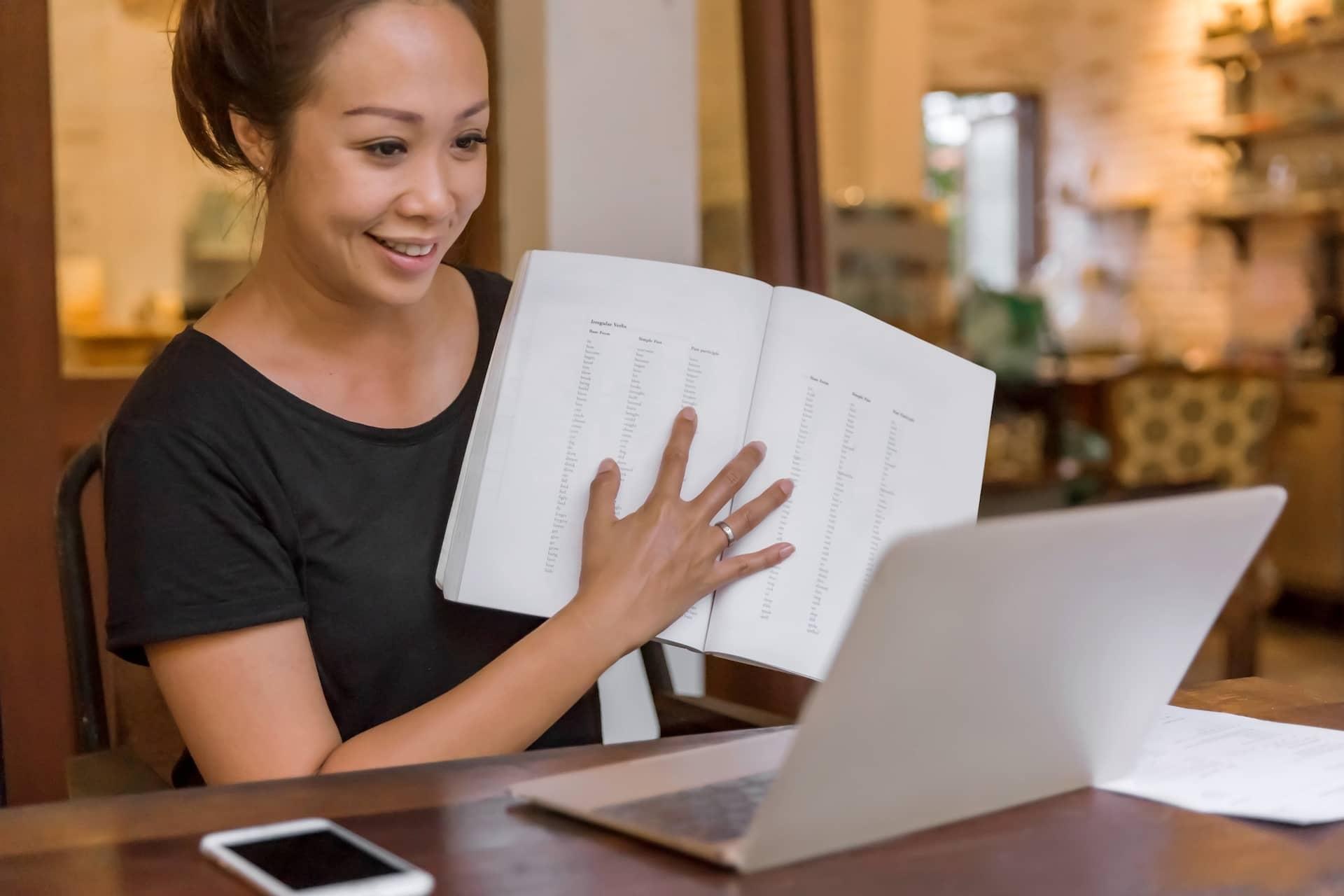 Woman holding up notebook to laptop computer
