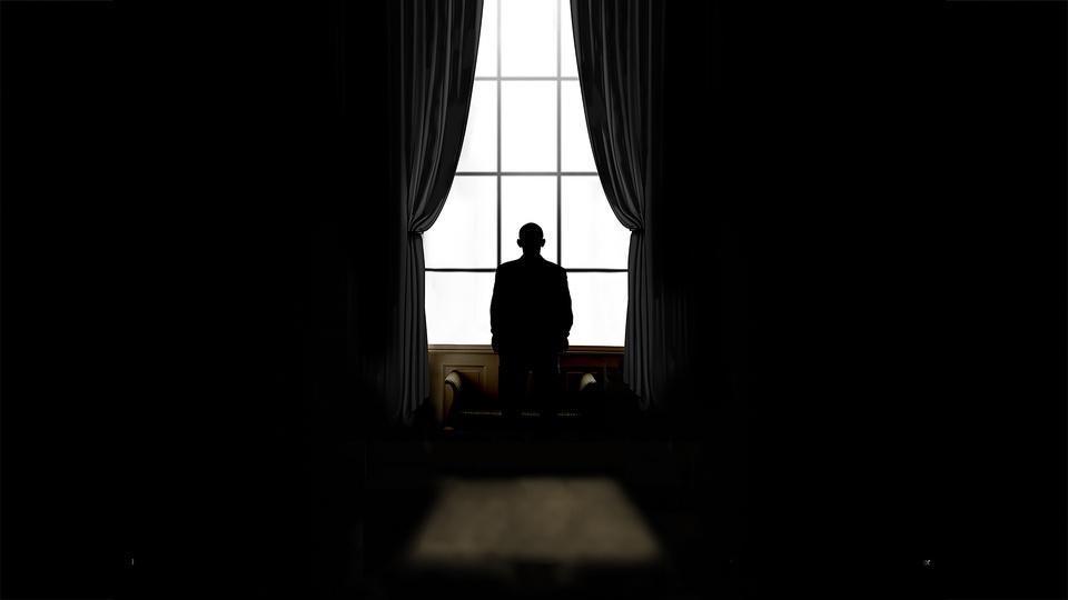 A figure in silhouette looking out a window in a dark room.