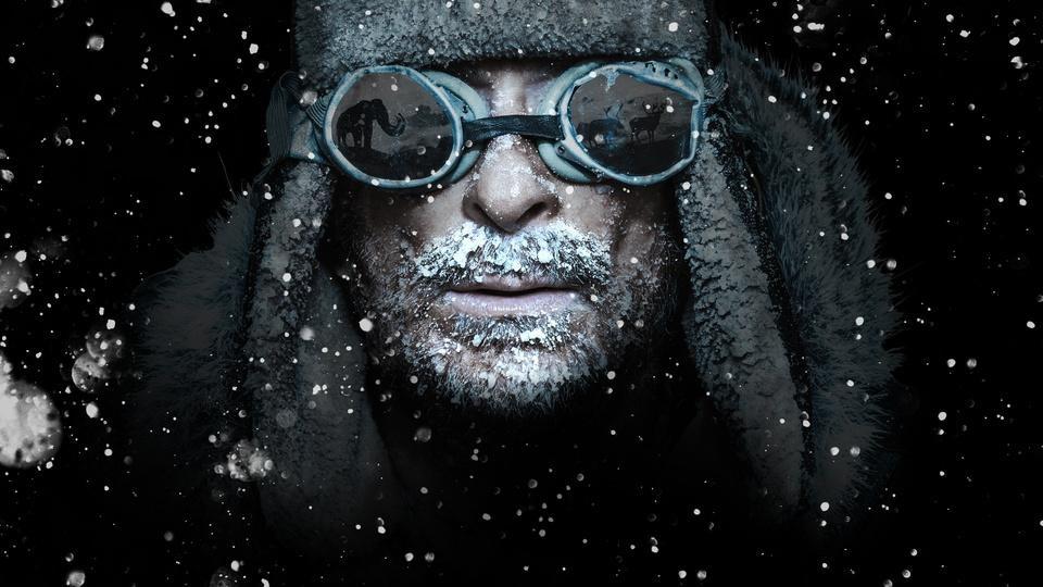 A man in the snow with prehistoric animals reflected in his goggles.