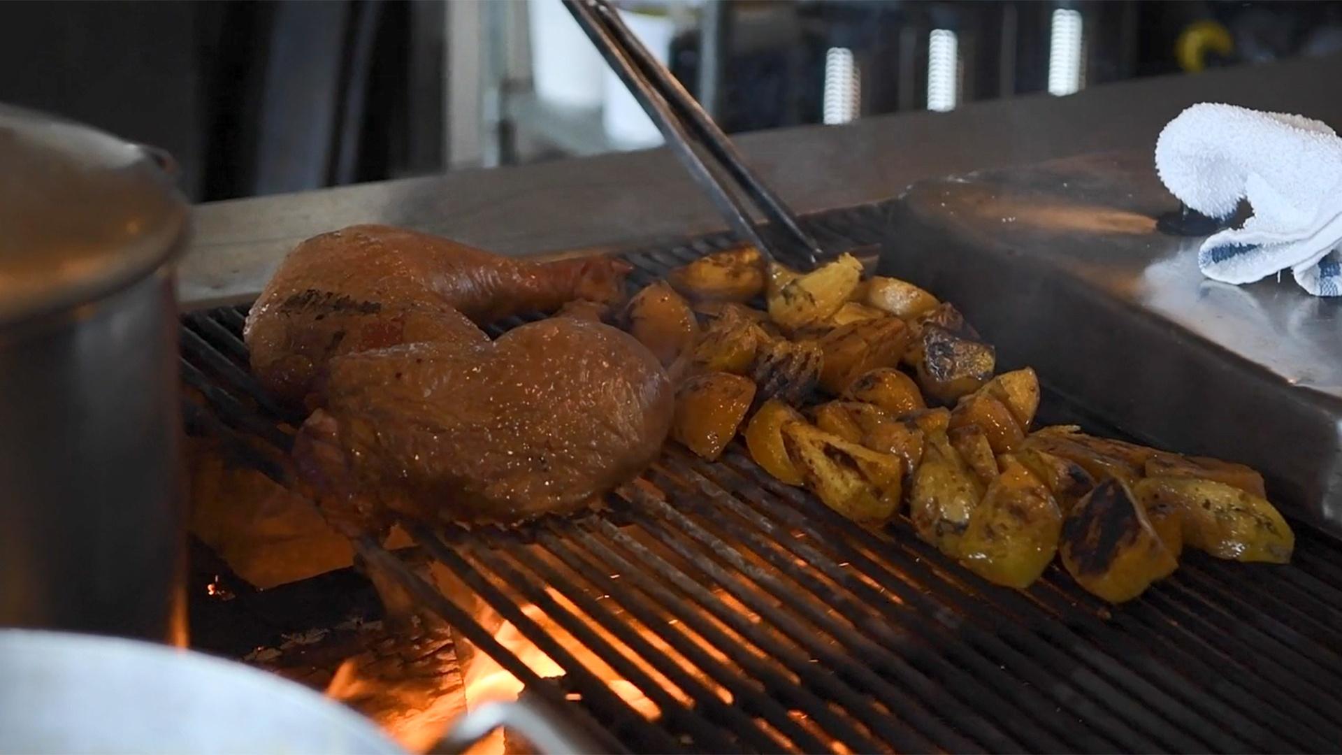 Chicken legs and vegetables cooking on a wood-fired grill.