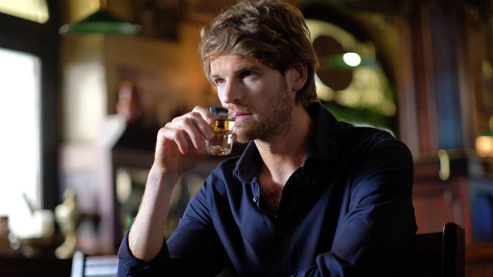 Maigret holding a shot glass to his lips.