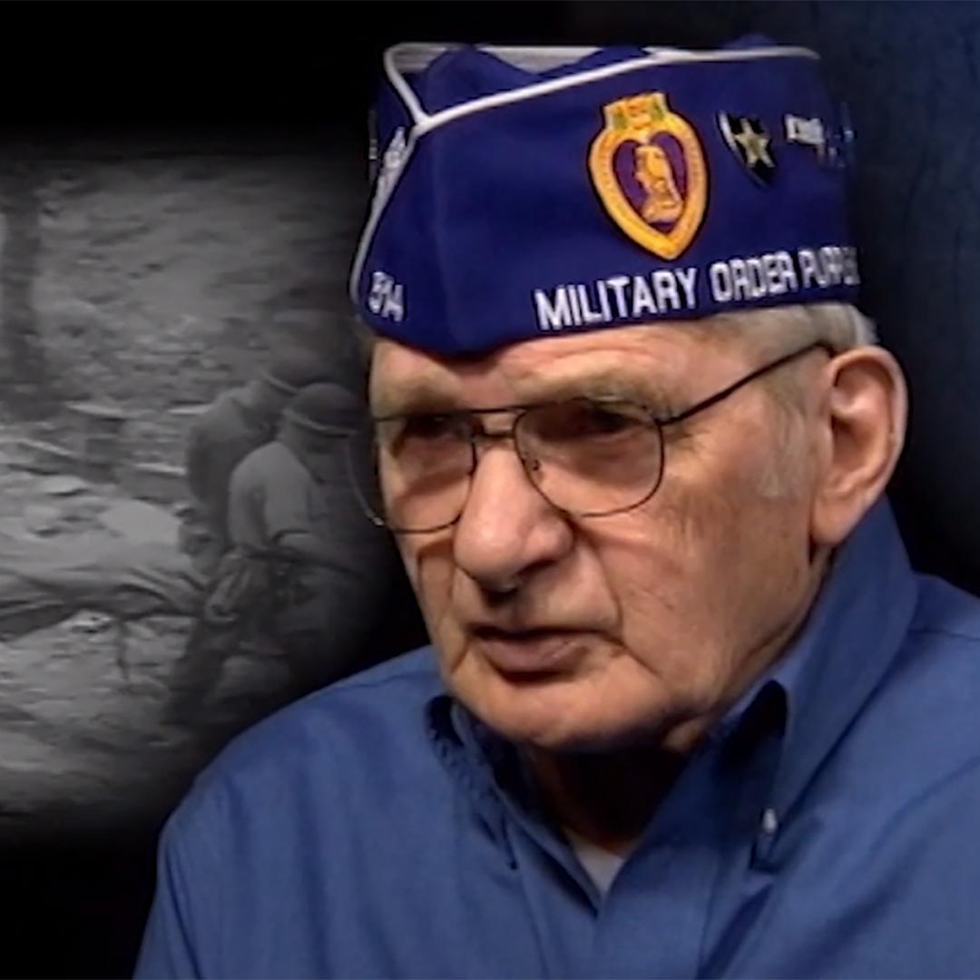 A Korean War veteran in an interview with images of the war projected behind him..