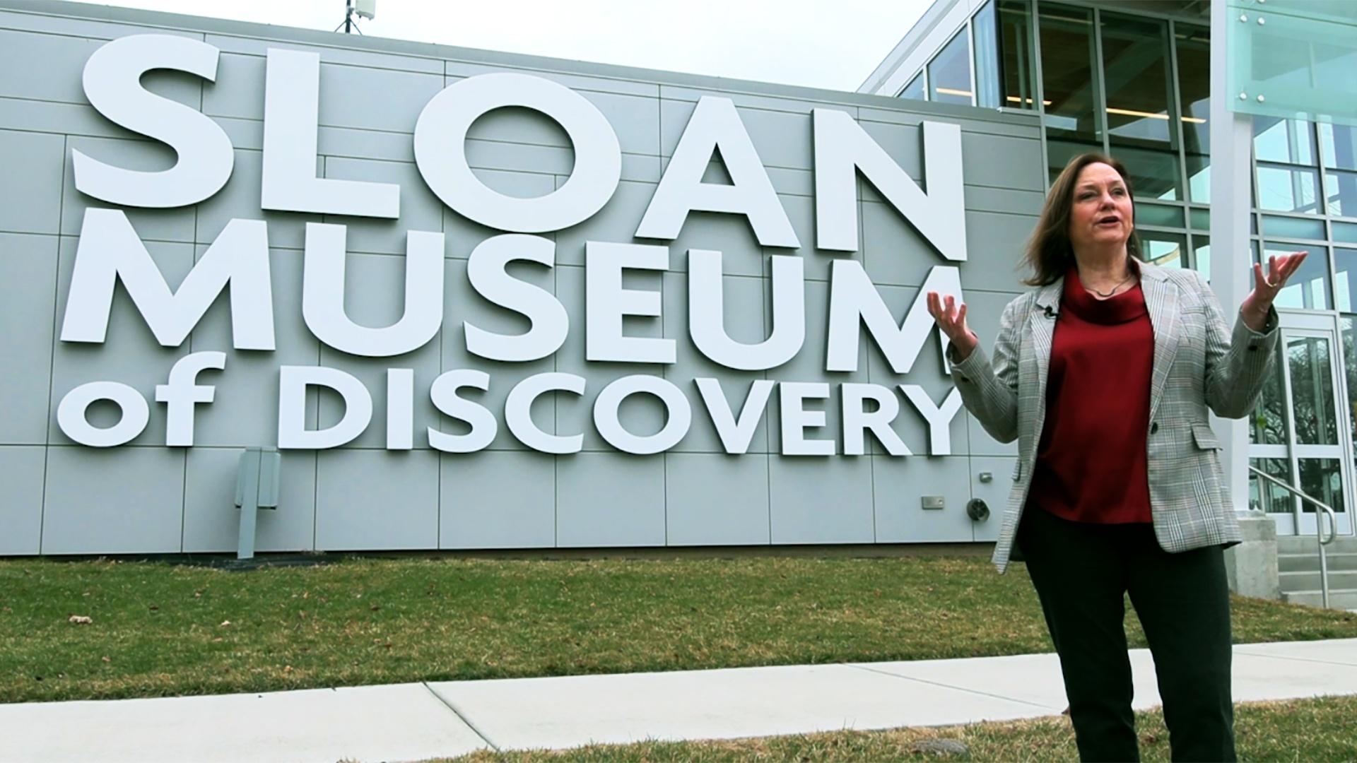 A woman stands in front of the Sloan Museum of Discovery.