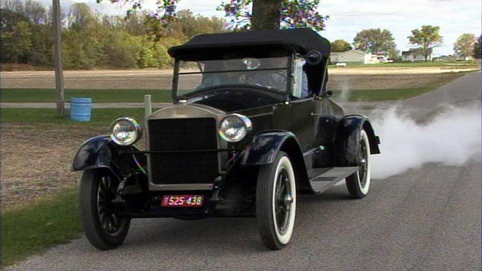 An antique car driving down a country road.