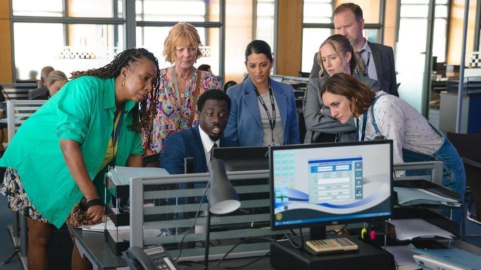 Becks, Suzie, and Judith crowd around a computer screen with the police.