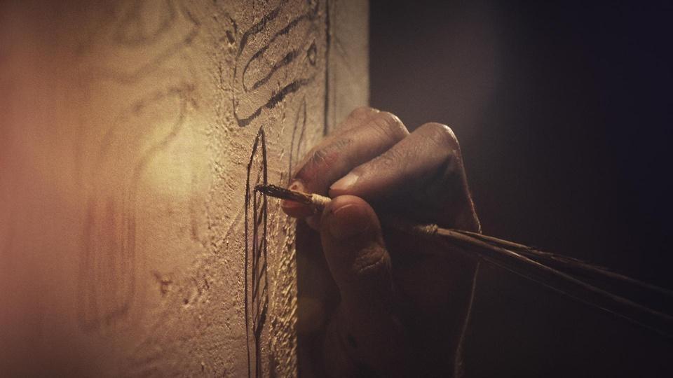 A closeup of a hand writing on a wall with a quill pen.