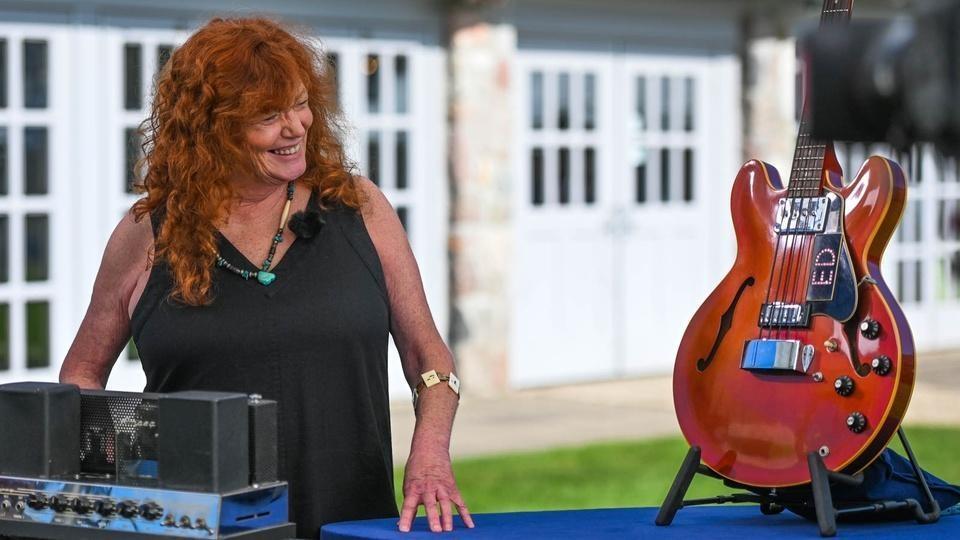 A woman stands next to her vintage guitar and amplifier.