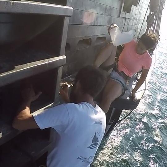 El Galeon crew members hang on to the side of the ship as they paint it.
