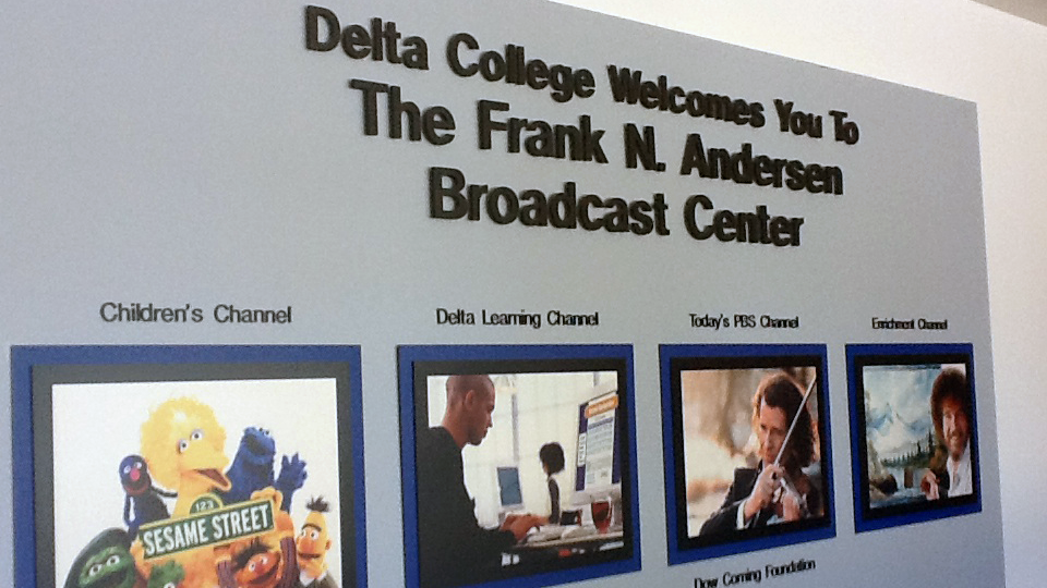 A sign that says "Delta College Welcomes You to the Frank N. Andersen Broadcast Center" with pictures of programming from four TV channels.