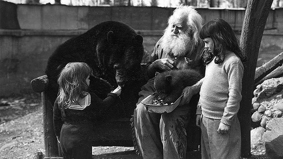 Two young girls feed an adult bear as Spikehorn sits with a bear cub on his lap.