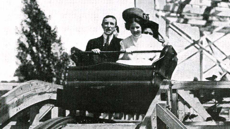 A couple rides a wooden roller coaster.