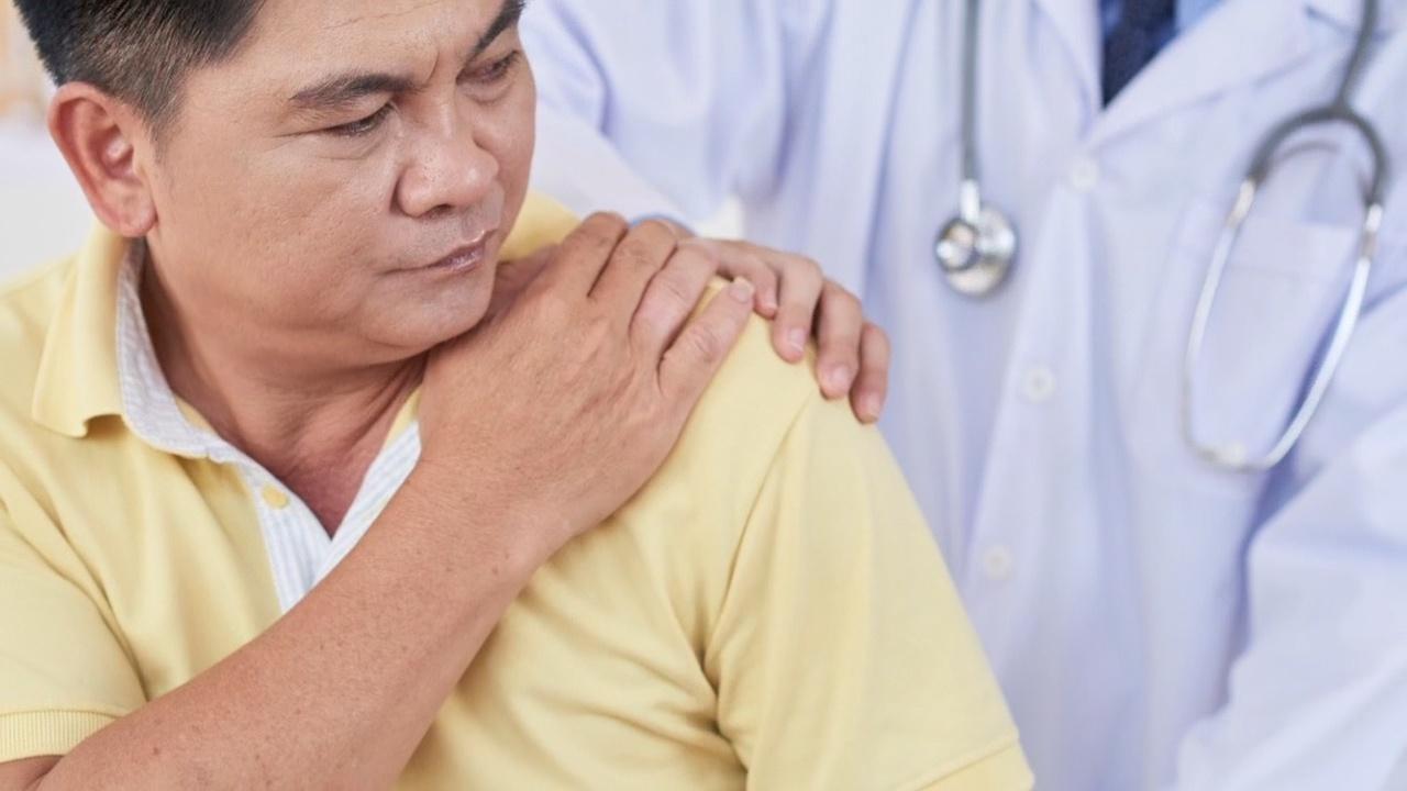 A man holds his shoulder in pain as a doctor examines it.