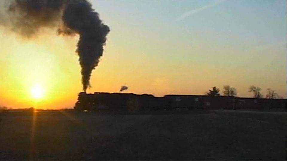 A freight train rolls through the countryside at sunset.