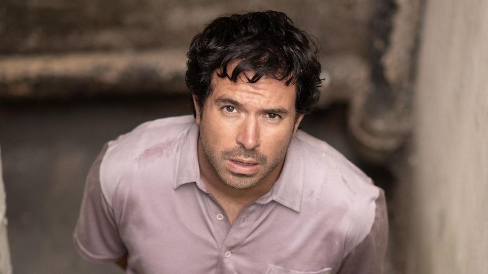 John Palmer stands in a basement looking up toward the camera.