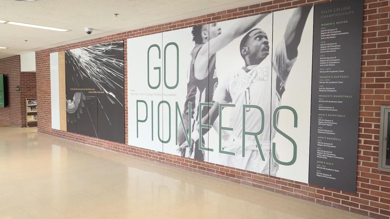 A sign at Delta College with two men playing basketball that says, "Go Pioneers."