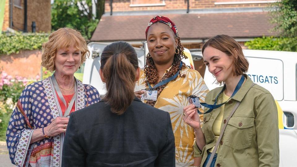 Judith, Suzie, and Becks show their badges to a woman.