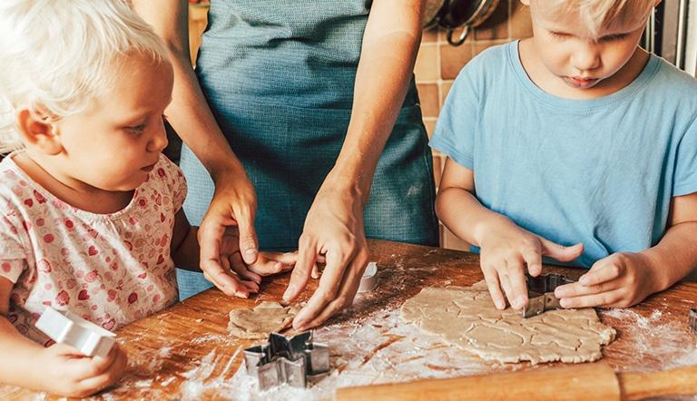 Two young children helping their mother bake cookies