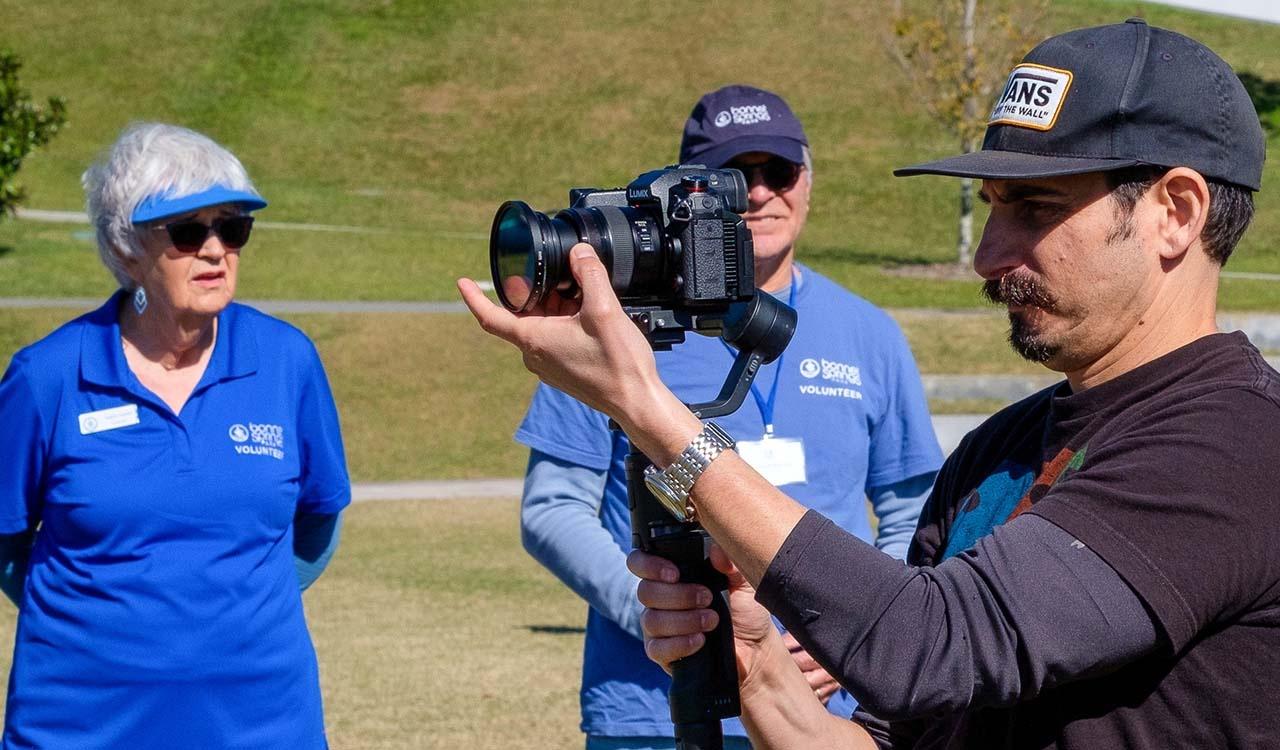 Triforce cameraman setting up a tripod and camera with two voluneteers in the background