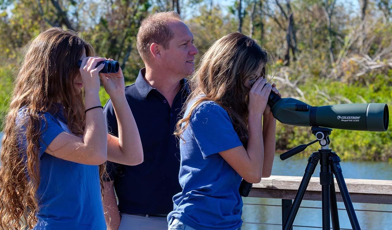 Three individuals, two are looking through scoping devices in the park