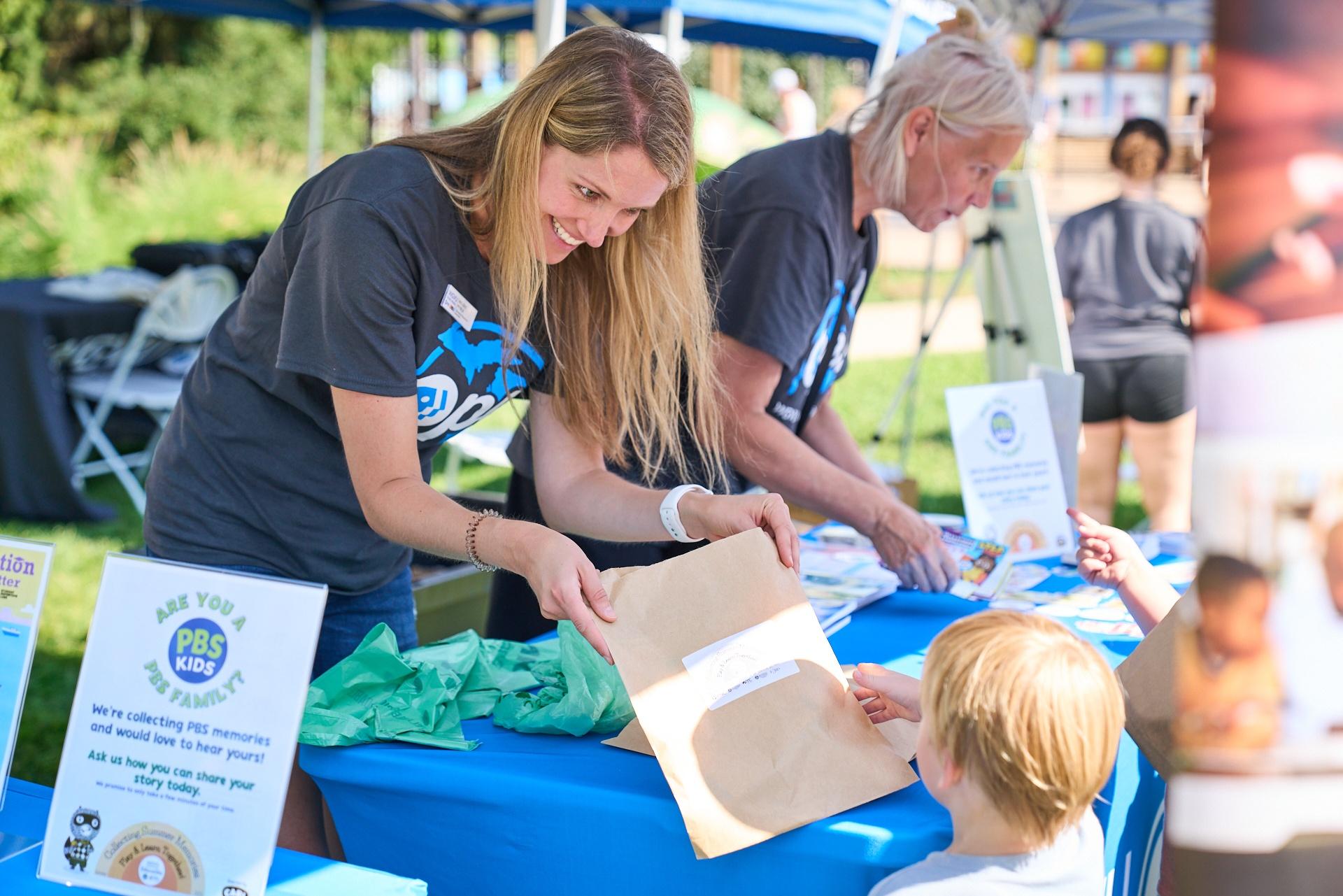 WGVU employees hand activity envelopes to children at an educational event