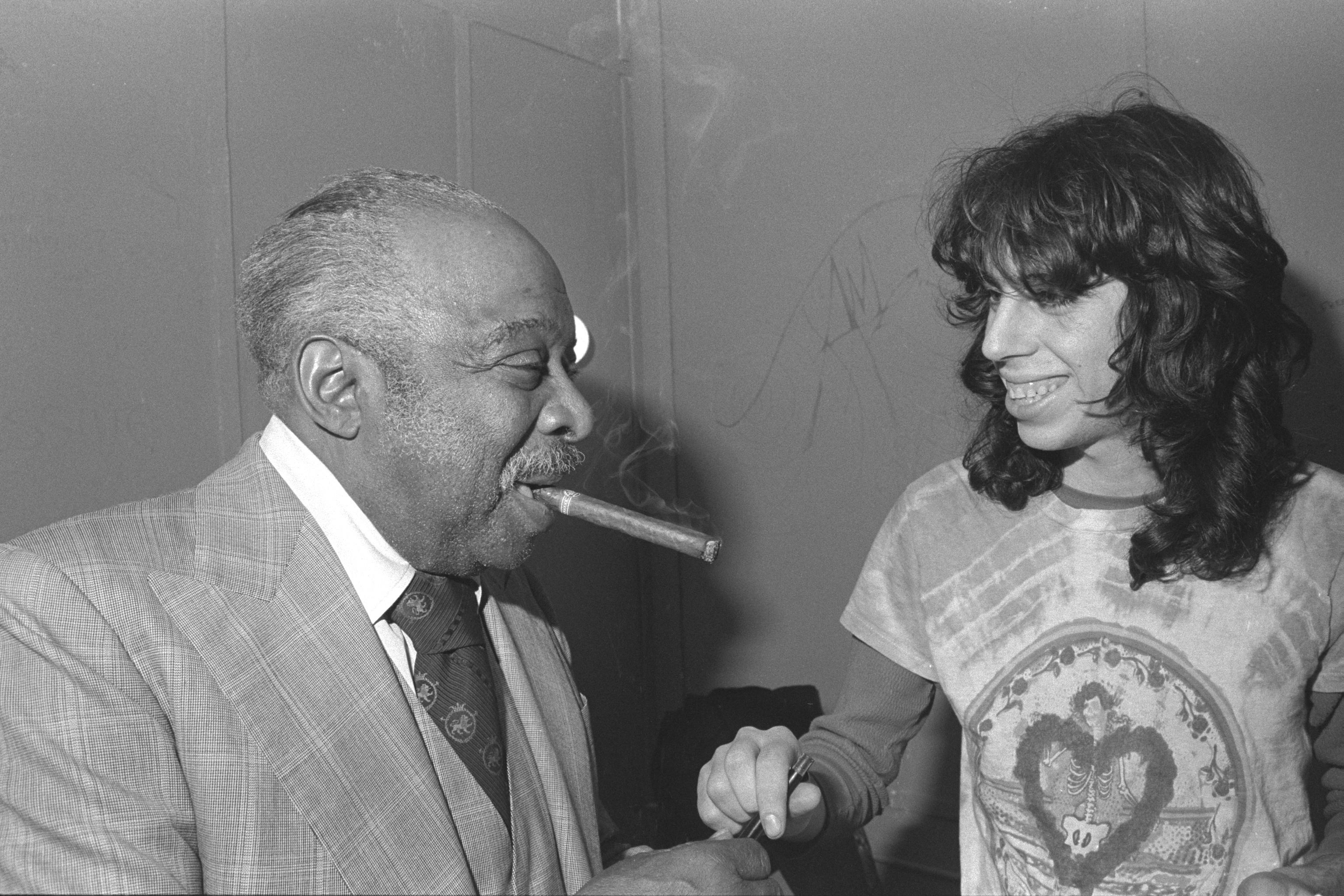 A black and white photo of Count Basie, with a cigar in his mouth, speaking with a fan at J.B. Scott's.
