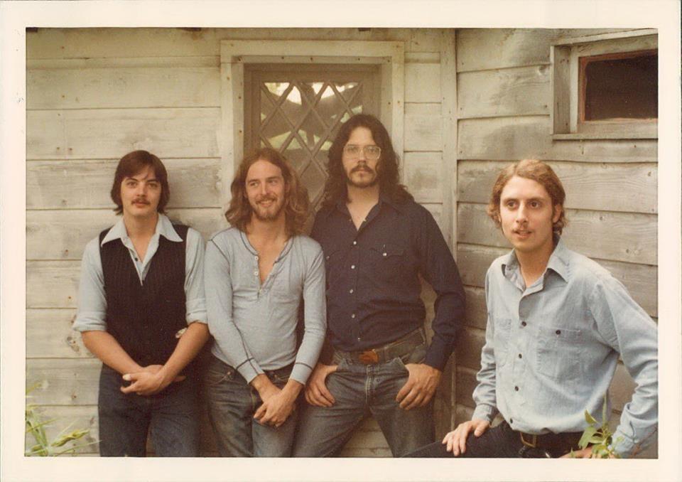 The band Silver Chicken posing in front a house with worn wooden siding.