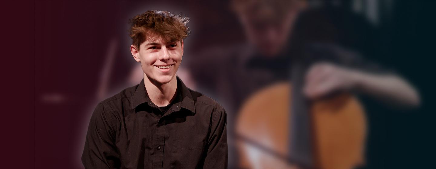 March 2021 Student Musician of the Month: Cellist Ethan Wilson sitting, wearing a black shirt while smiling.