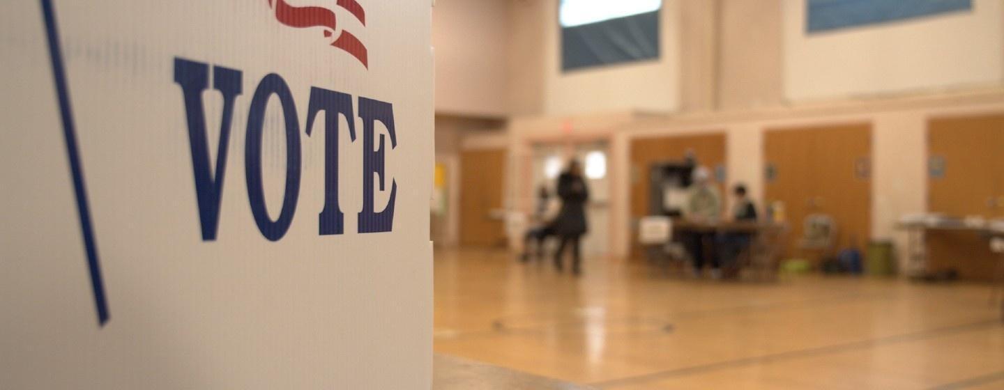 The side of a voting booth is shown. The pictured polling place is located inside if a gymnasium.