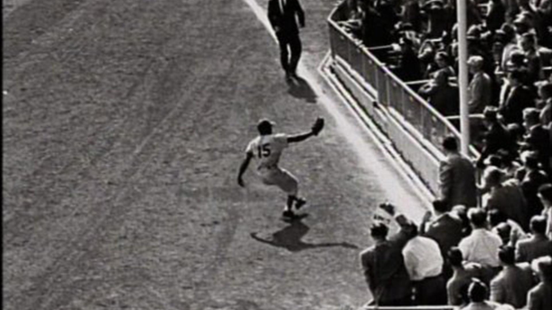A baseball player on a field reaches out his glove to catch a fly ball.
