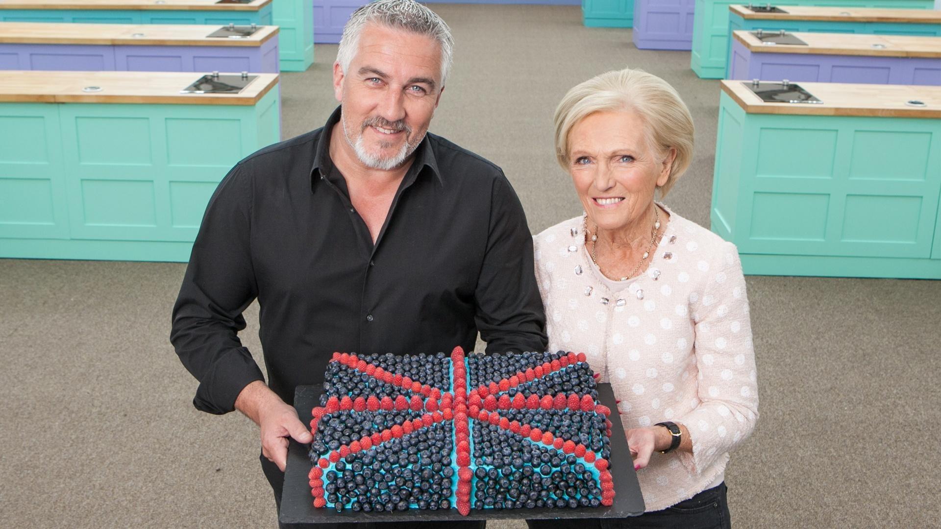 Paul Hollywood and Mary Berry hold a cake with berries on it that looks like the United Kingdom flag.