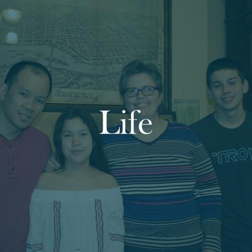 The word "life" is displayed in white, serif, type on a dark green transparent overlay on top if an image of Thanh and his family.