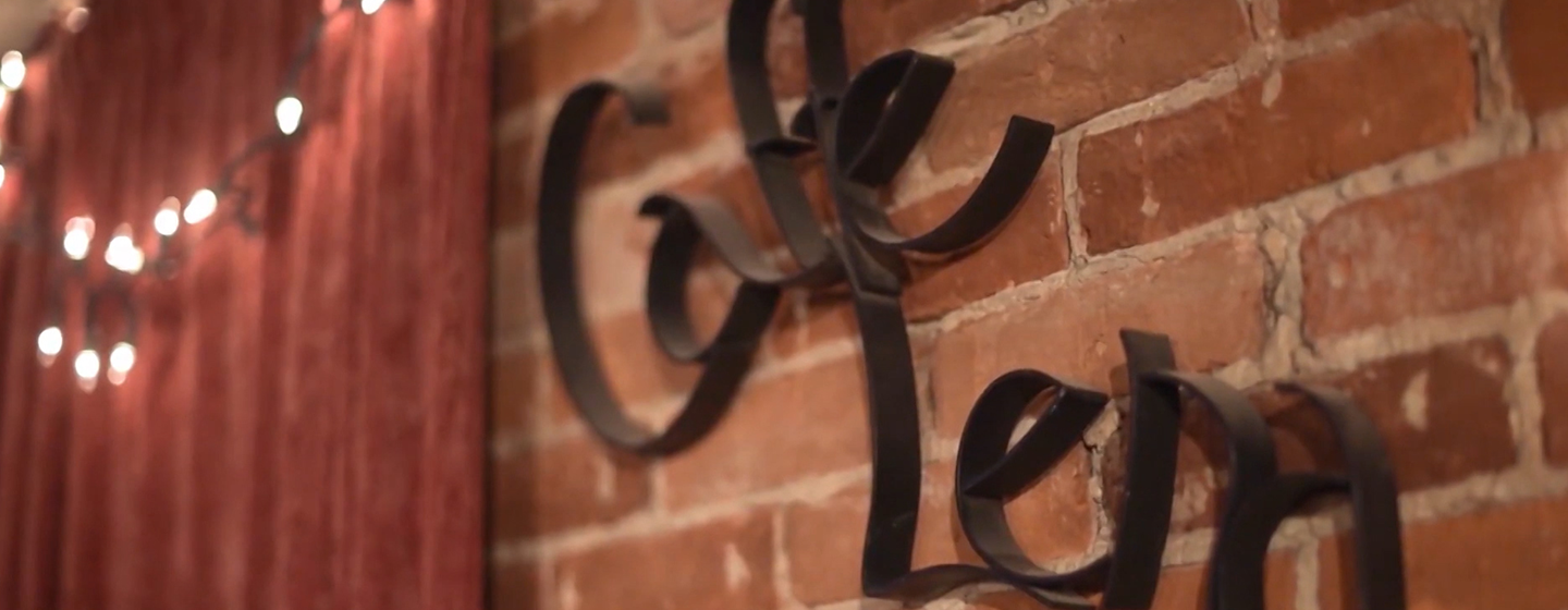 The iron Caffe Lena Sign sits on a brick wall in the performance space at the caffe