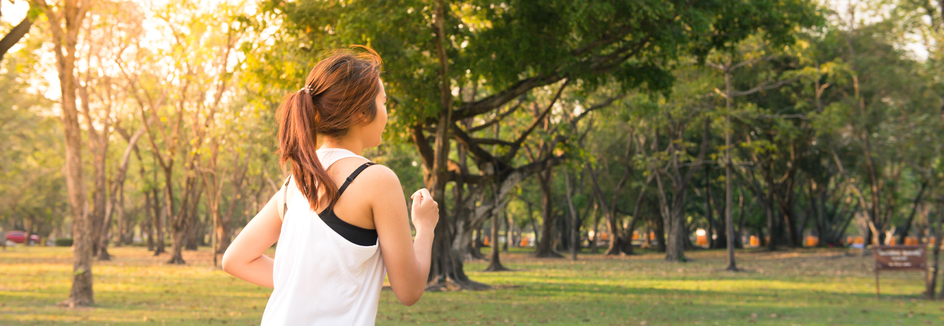 A woman in athletic apparel is seen jogging through a wooded area.