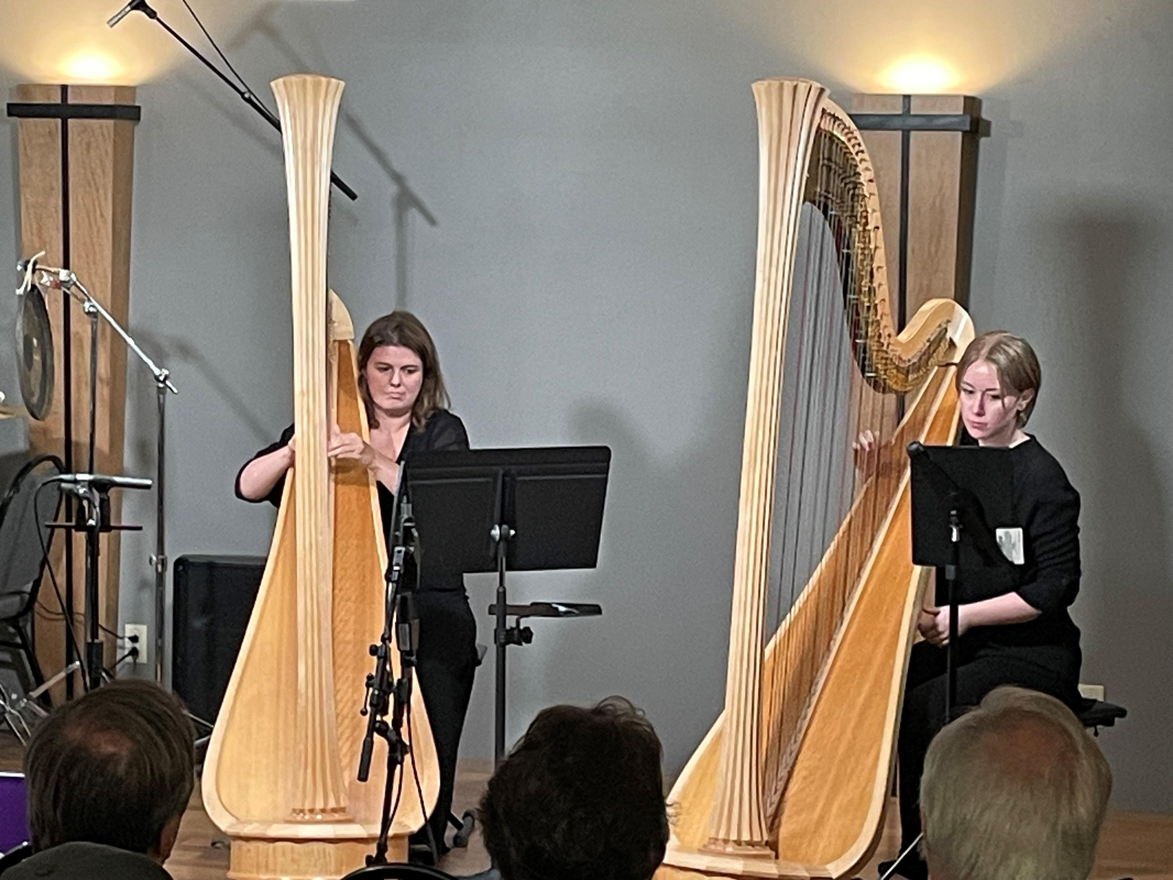 Two women performing on stage, one playing a harp