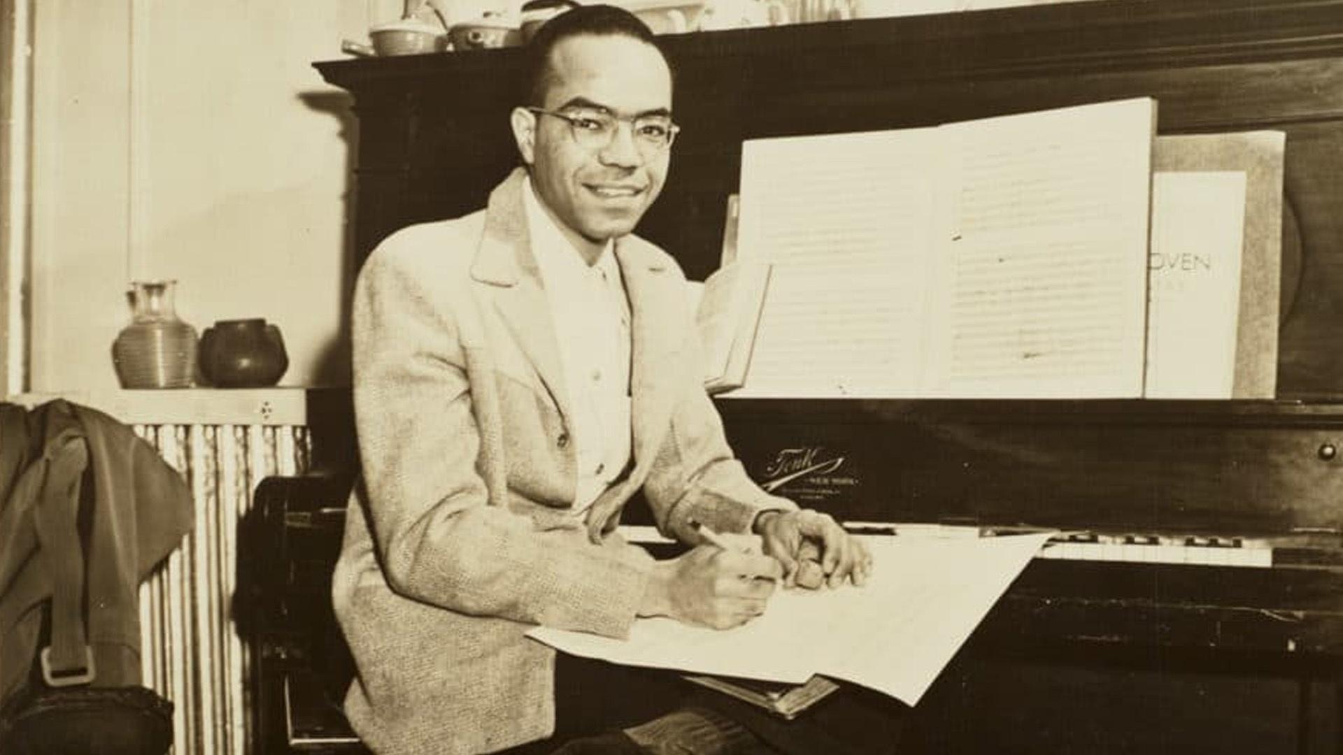 Composer Ulysses Kay sitting in front of a piano and holding a pen and paper in an undated photo.