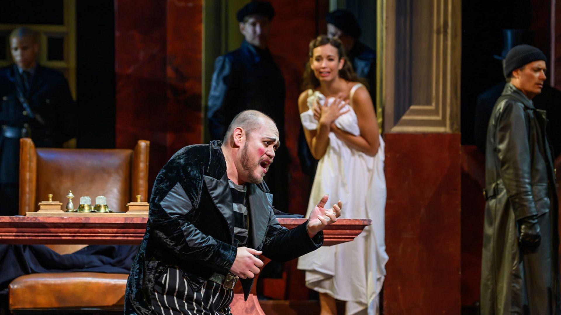 A scene from "Rigoletto" where a man is singing on his knees, with a petrified woman in the background